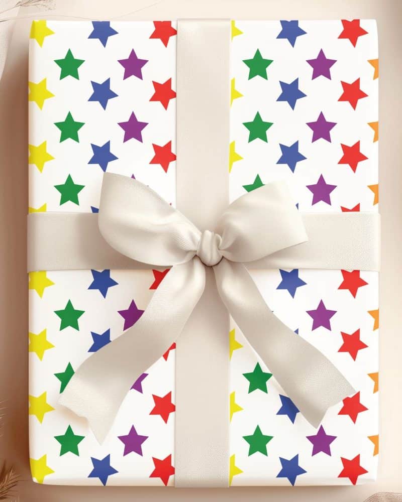 A gift wrapped in white paper with a rainbow star pattern and a large off-white bow.