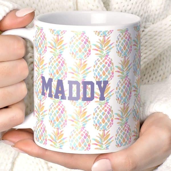 A White Coffee Mug With A Pastel Pineapple Pattern And The Name Maddy In Purple.