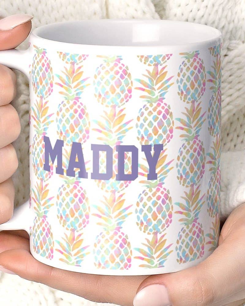 A white coffee mug with a pastel pineapple pattern and the name Maddy in purple.