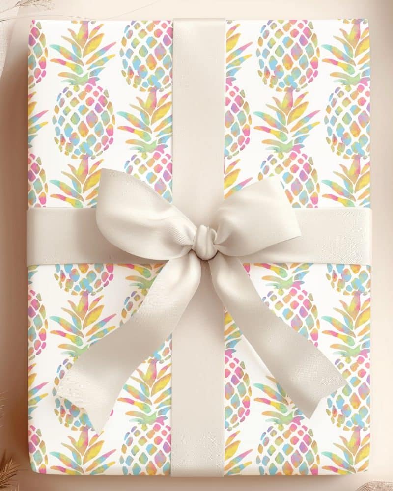 A gift wrapped in white paper with a pastel rainbow pineapple pattern and a cream-colored ribbon.