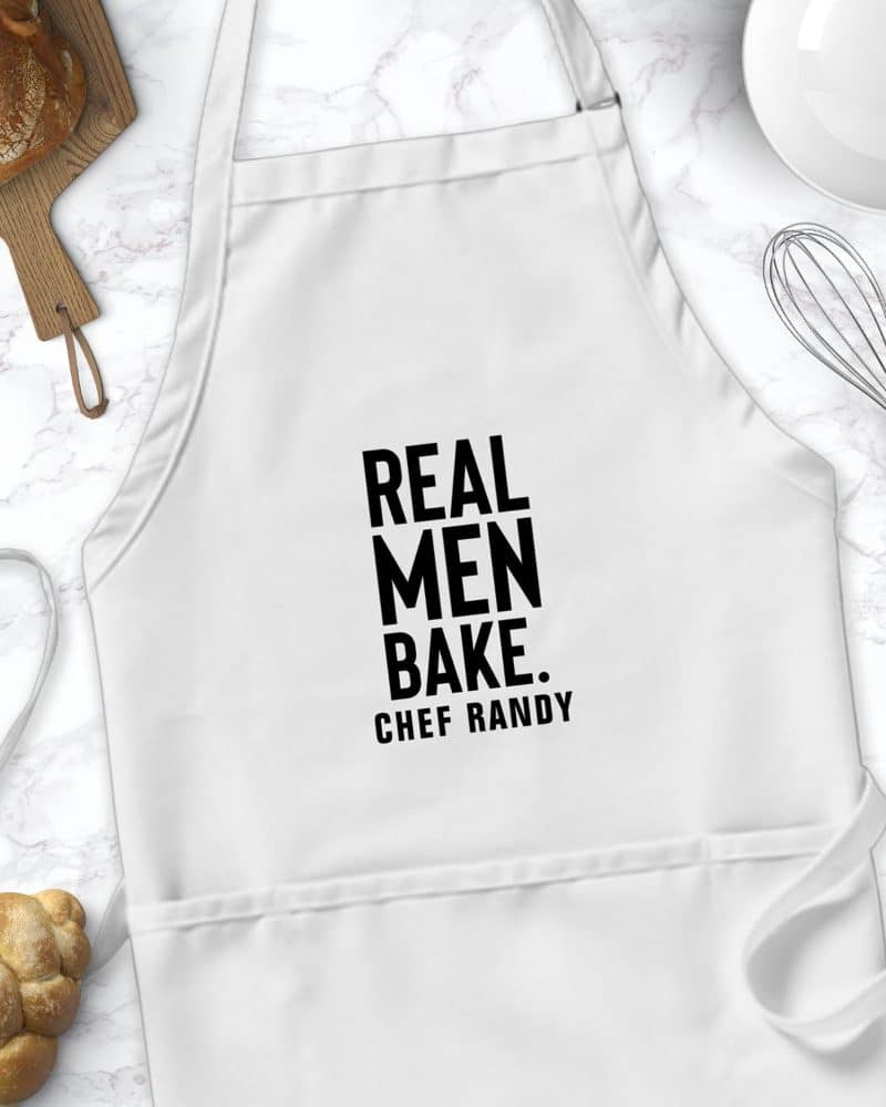 White apron with the text Real Men Bake. Chef Randy.