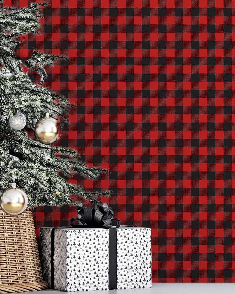 A decorated Christmas tree and a gift sit in front of a red and black buffalo plaid background.
