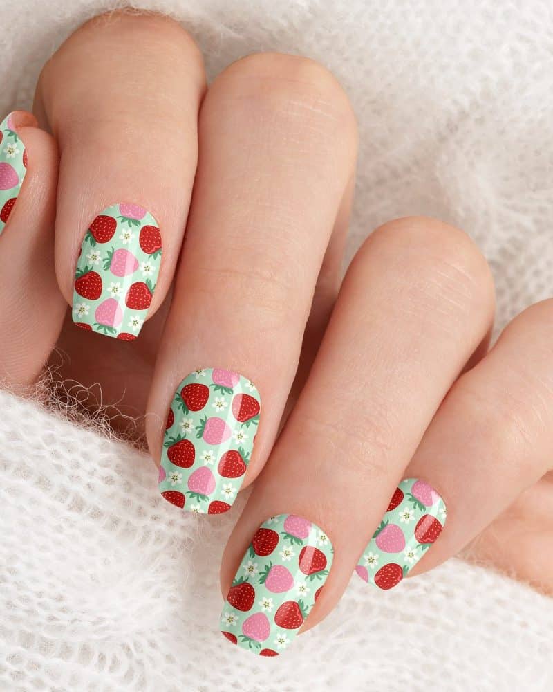 Close-up of a hand with fingernails decorated with a strawberry pattern.