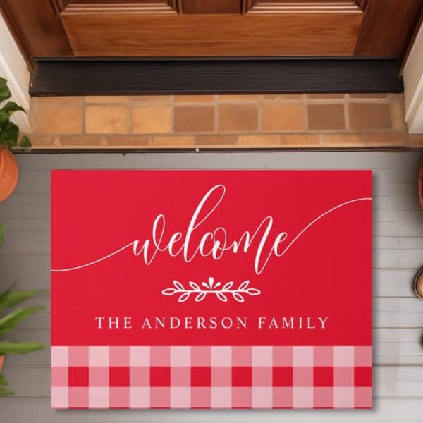 Red Welcome Mat With White Script Lettering That Says Welcome, A Small Floral Design, And The Anderson Family. The Bottom Features A Red And Pink Gingham Pattern.
