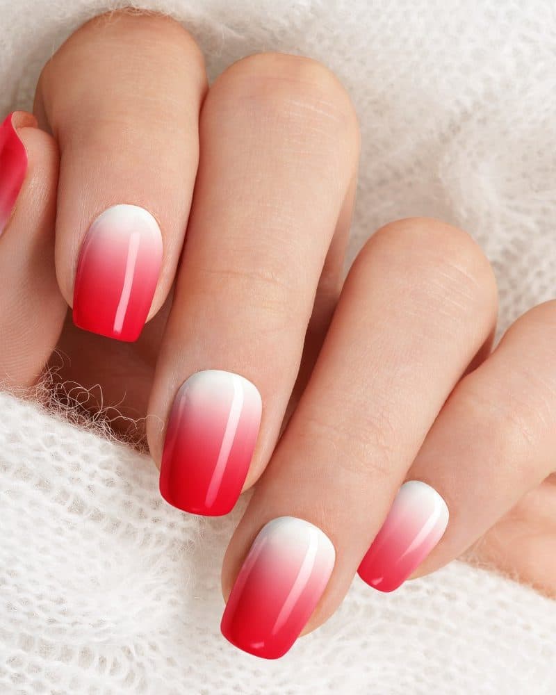 Close-up of a hand with ombre nails, transitioning from white to bright red.