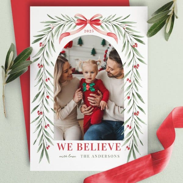 Christmas Card Featuring A Family Photo Of Parents And Their Toddler Framed By A Watercolor Arch Of Greenery And Berries. The Year 2025 And The Family'S Name, The Andersons, Are Included.