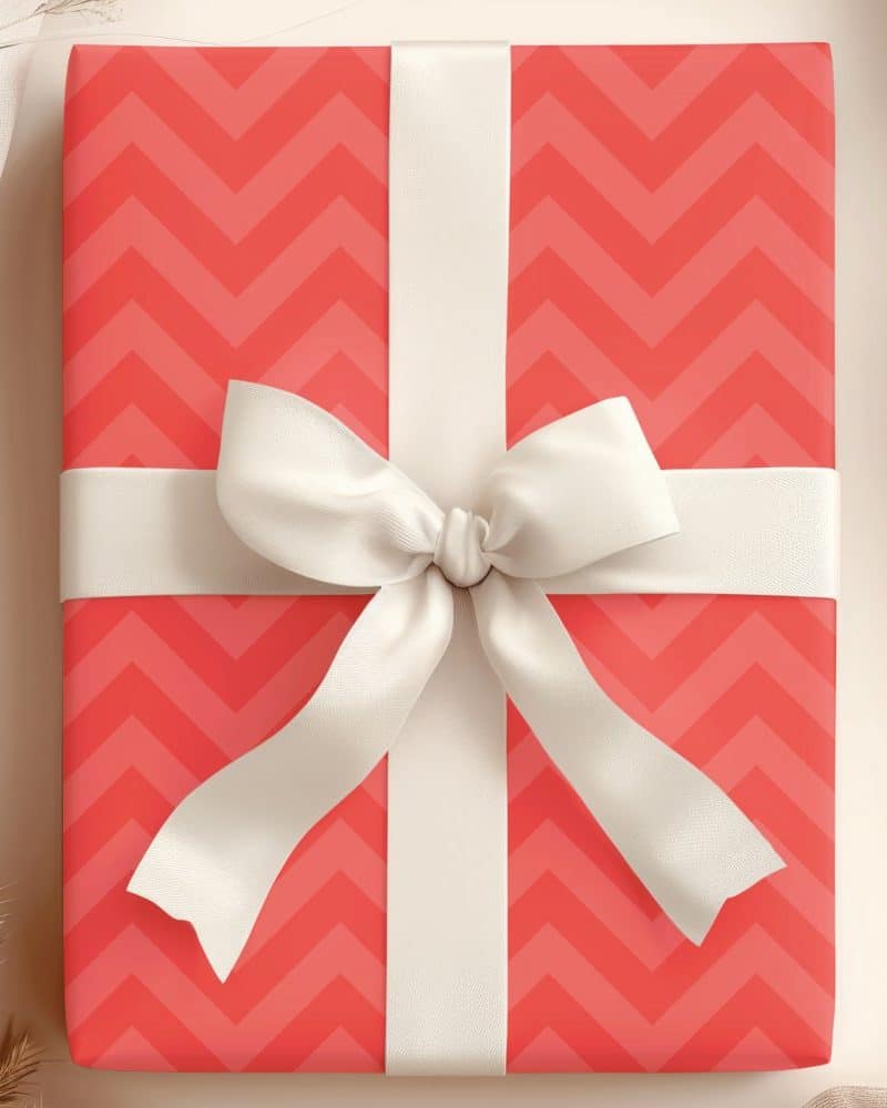 A coral pink gift box with a white chevron pattern and large white bow.