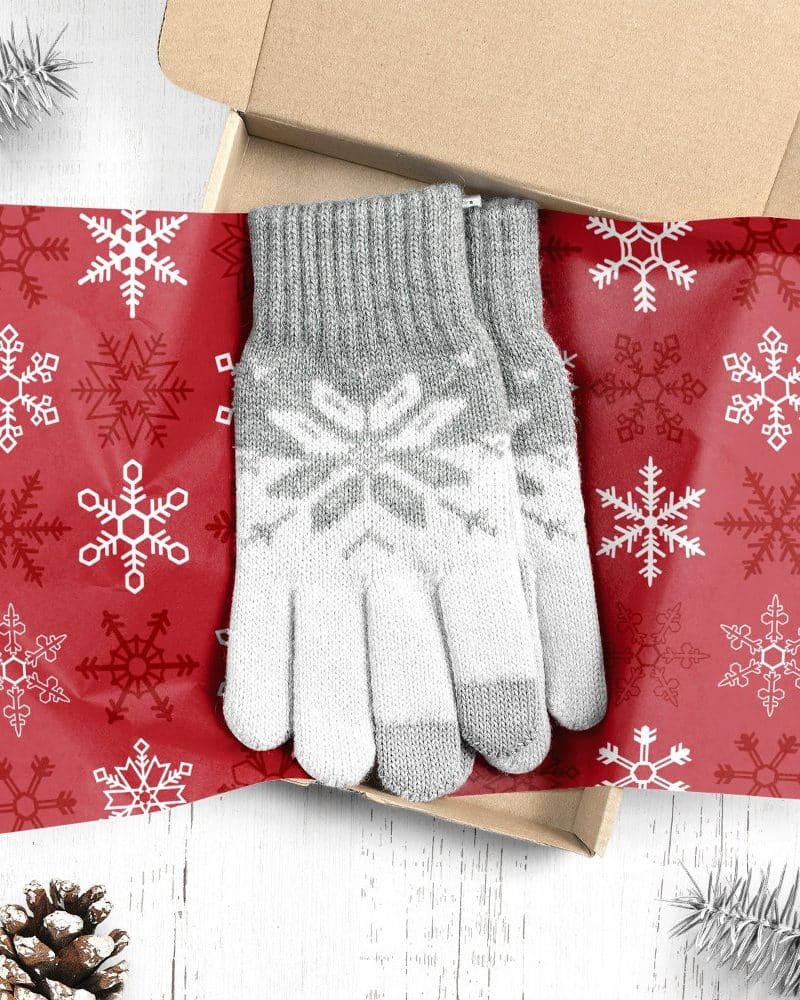 Pair of gray and white knit gloves with snowflake pattern, in a gift box lined with red snowflake wrapping paper.