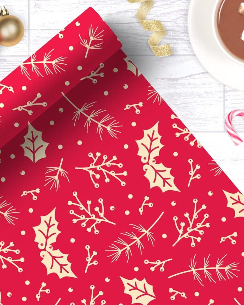 Red Christmas wrapping paper with a pattern of cream-colored holly leaves and pine branches.