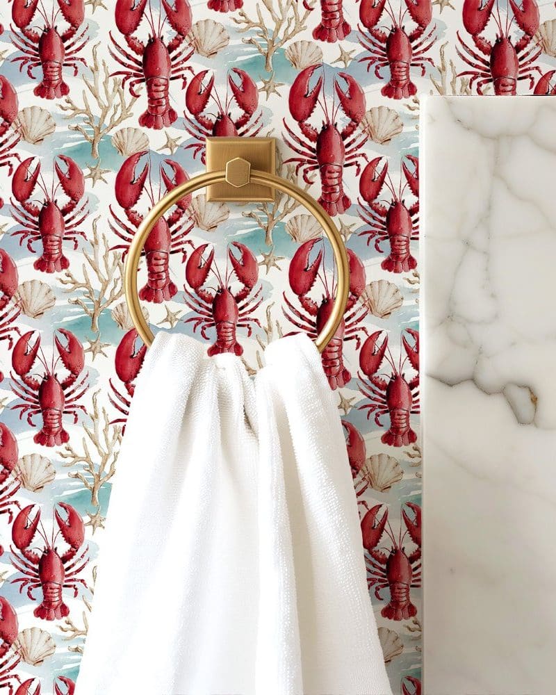 White towel hanging on a gold ring against a wallpaper of red lobsters and seashells.