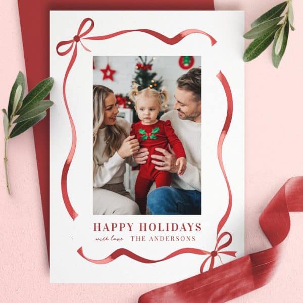 Christmas Card Featuring A Family Photo Of Parents And Their Toddler Daughter. A Red Ribbon Border Frames The Image.