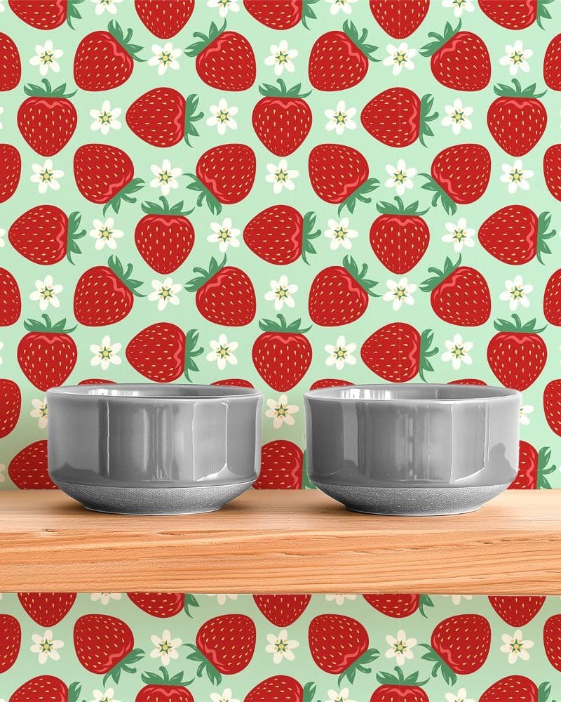 Two gray bowls sit on a wooden shelf in front of a strawberry wallpaper.