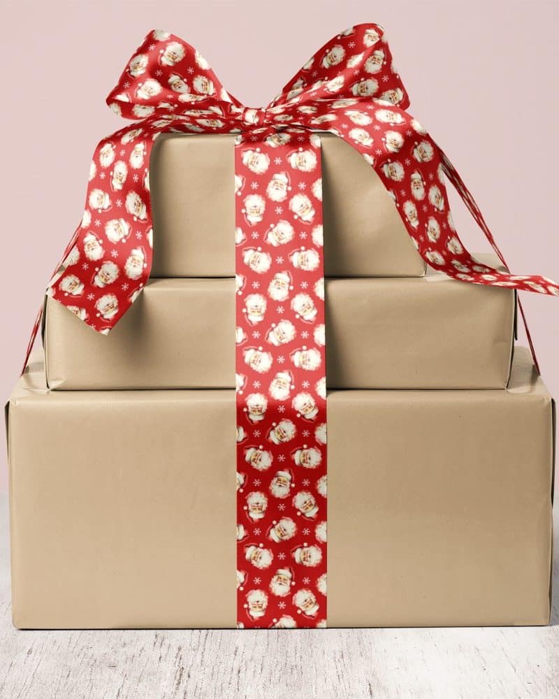 A stack of three brown gift boxes tied with a red ribbon featuring a Santa Claus pattern.