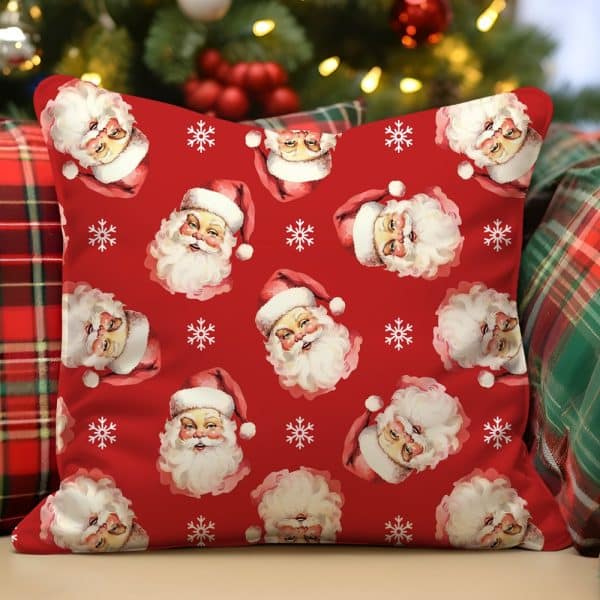 Red Throw Pillow With A Repeating Pattern Of Santa Claus Faces And Snowflakes.