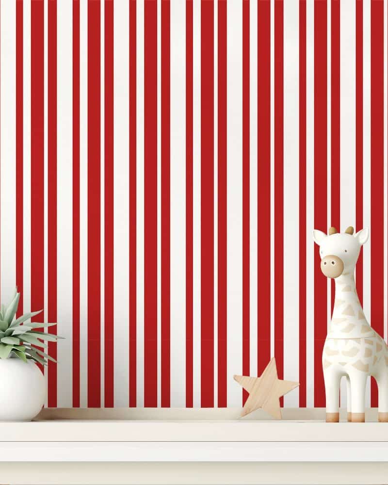 A white shelf holds a small giraffe toy and a small plant against a red and white striped wall.