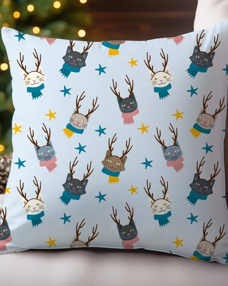 Light blue throw pillow with a repeating pattern of cats wearing antlers and scarves.