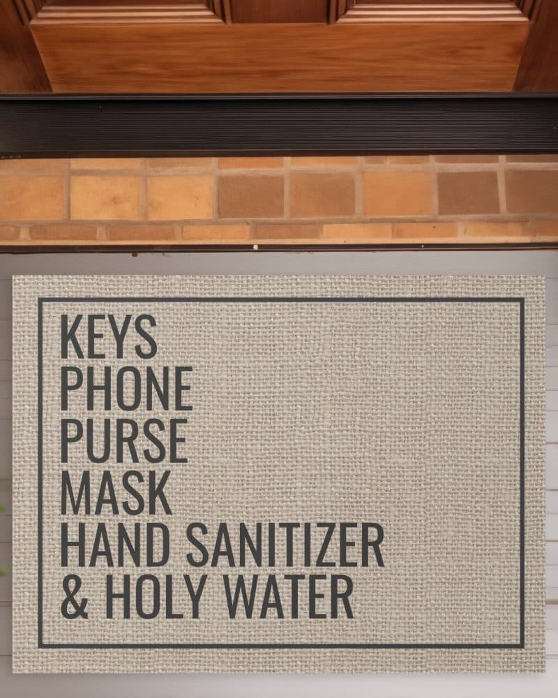 Tan doormat with black text listing keys, phone, purse, mask, hand sanitizer, and holy water.