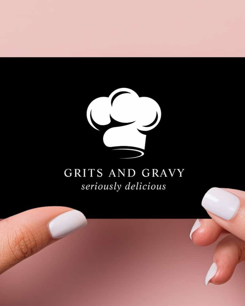 Two hands hold a black business card with a white chef's hat and the text Grits and Gravy seriously delicious.
