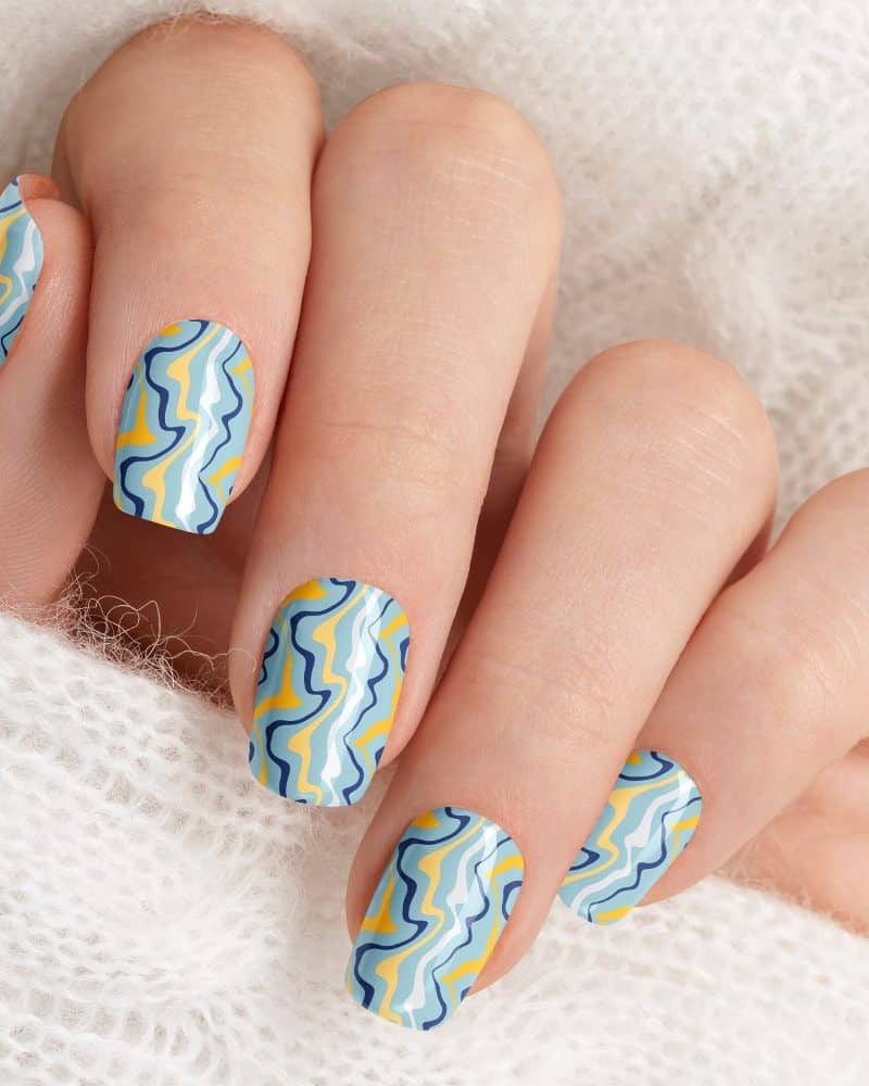 Close-up of a hand with light blue and yellow wavy nail polish.