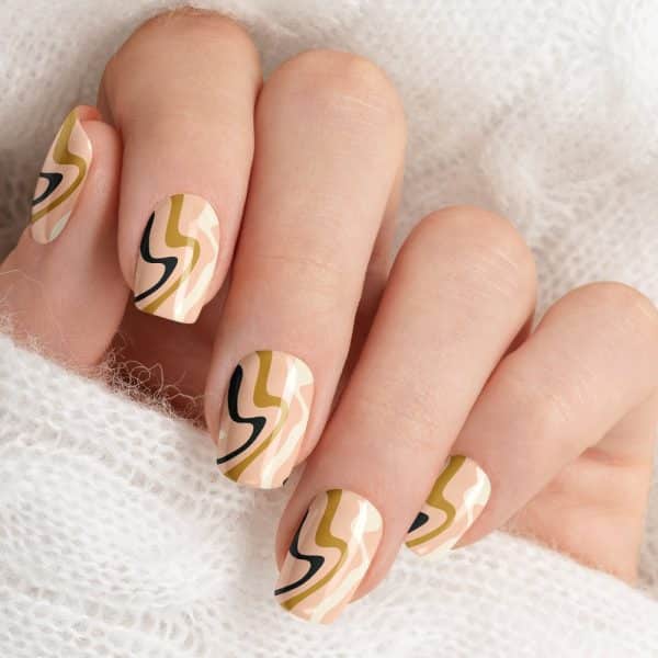 Close-Up Of A Hand With Nails Painted With An Abstract Design Of Wavy Lines In Beige, Gold, And Black.