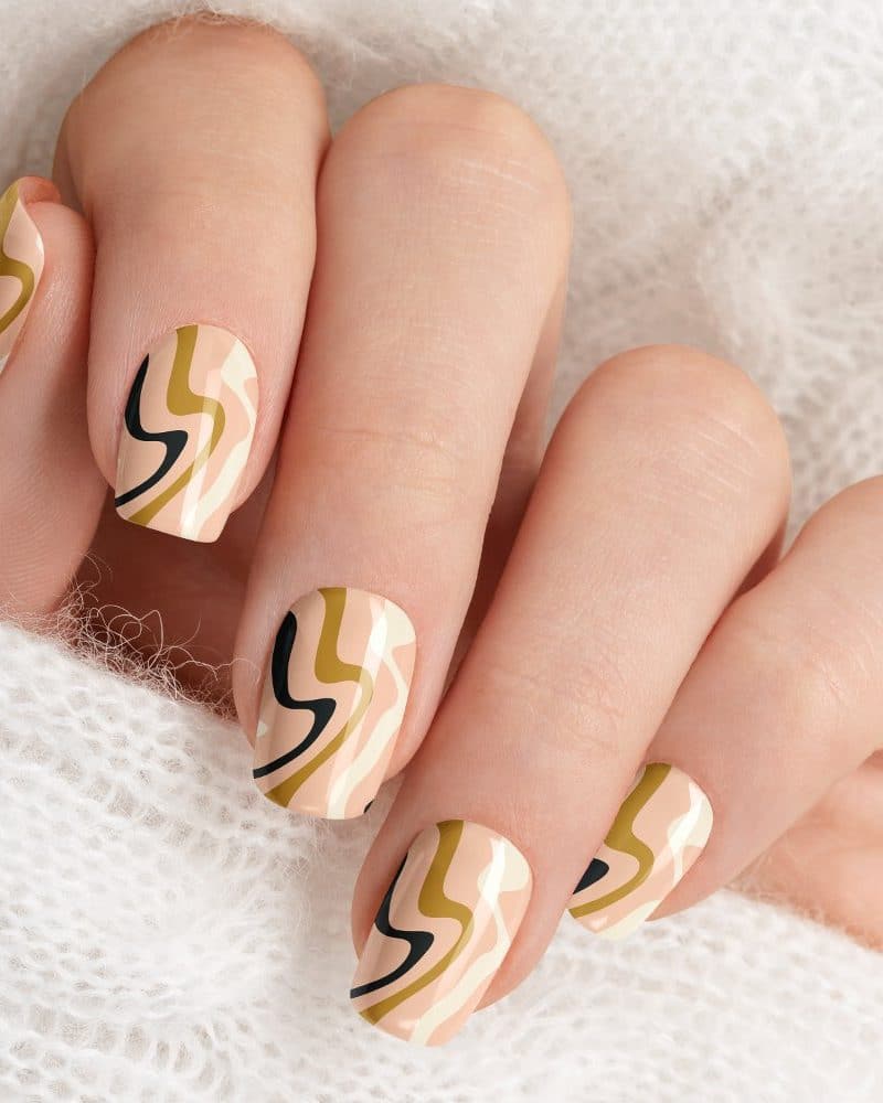 Close-up of a hand with nails painted with an abstract design of wavy lines in beige, gold, and black.