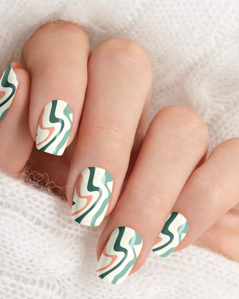 Close-up of a hand with fingernails painted with a wavy, abstract design in teal, cream, and peach.