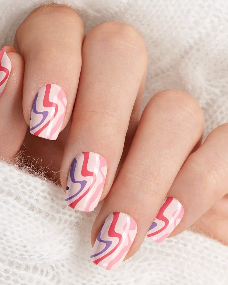 Close-up of a hand with pink nails featuring a wavy, abstract design in shades of pink, purple, and red.