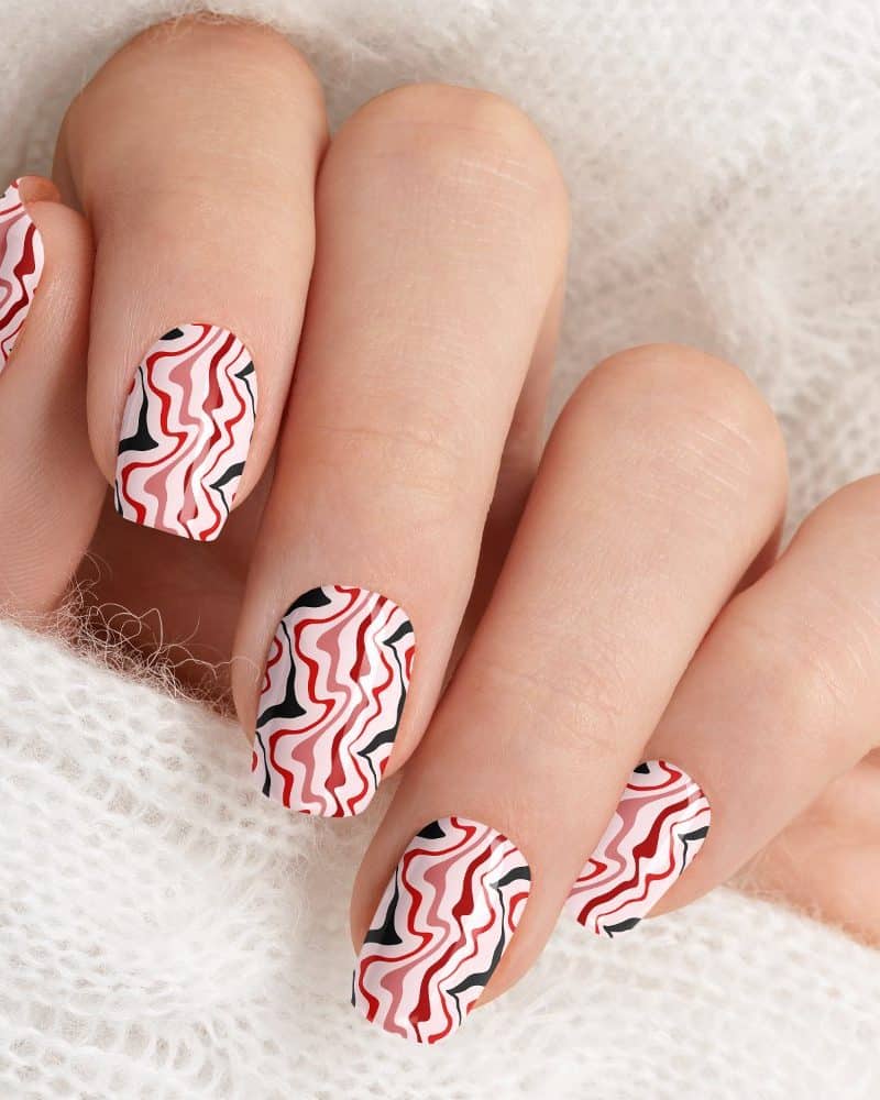 Close-up of a hand with nails painted with a red, pink, black, and white wavy pattern.