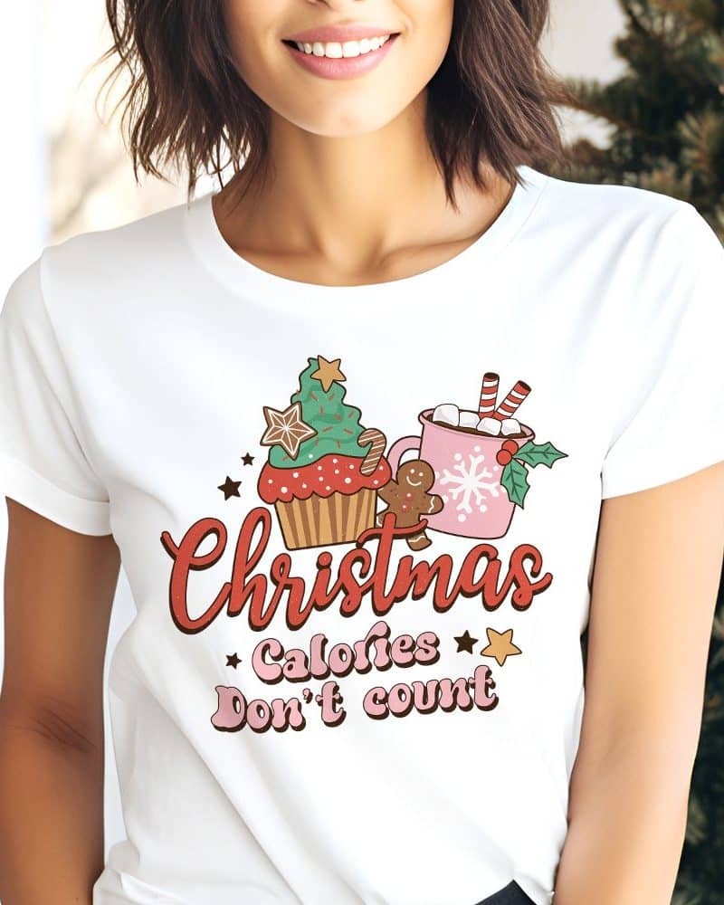 Woman wearing a white t-shirt with a Christmas design featuring a cupcake, hot chocolate, and gingerbread man, and the text Christmas Calories Don't Count.