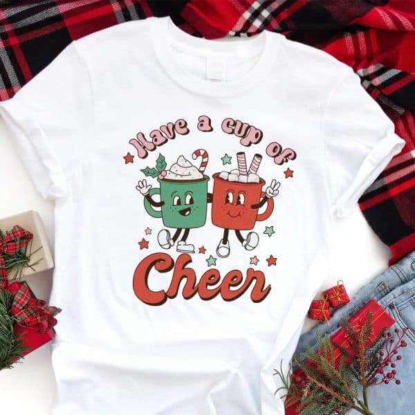 White T-Shirt With A Christmas Design Featuring Two Cartoon Mugs Holding Hot Chocolate, And The Text Have A Cup Of Cheer.