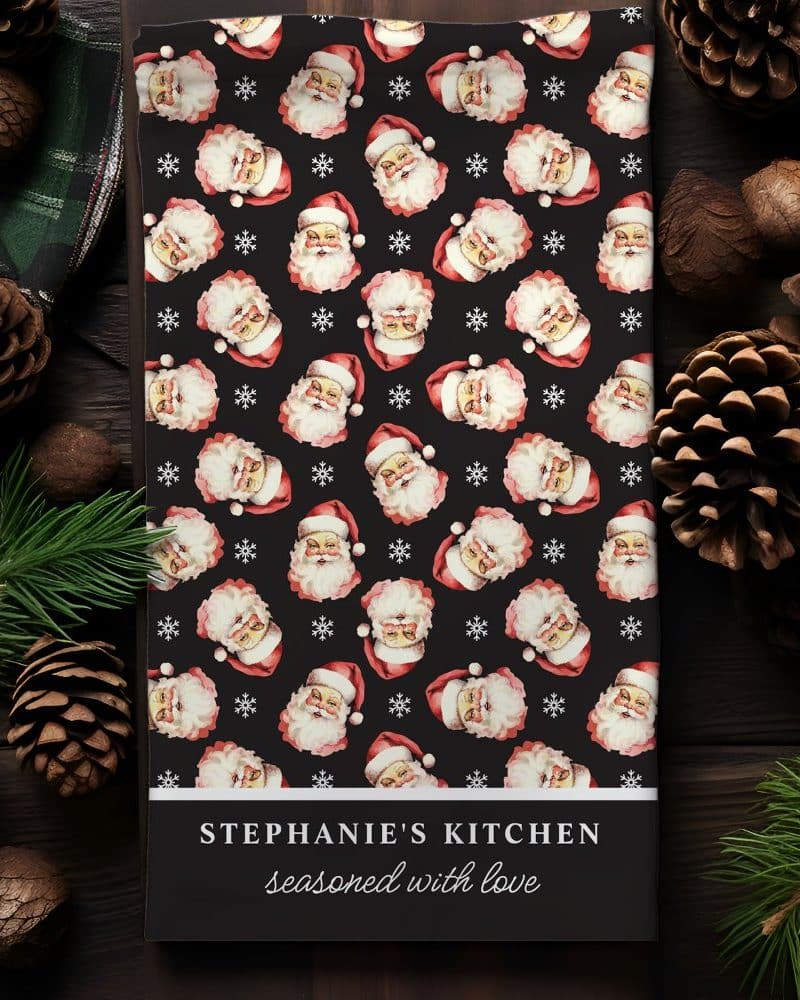 Christmas kitchen towel with a repeating pattern of Santa Claus faces, personalized with the name Stephanies Kitchen.