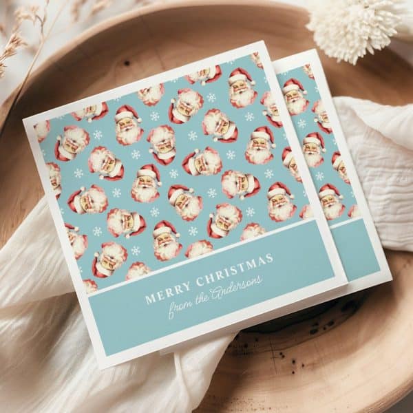 A Light Blue Christmas Card Featuring A Repeating Pattern Of Santa Claus Faces And Snowflakes. The Card Is Personalized With The Message Merry Christmas From The Andersons.