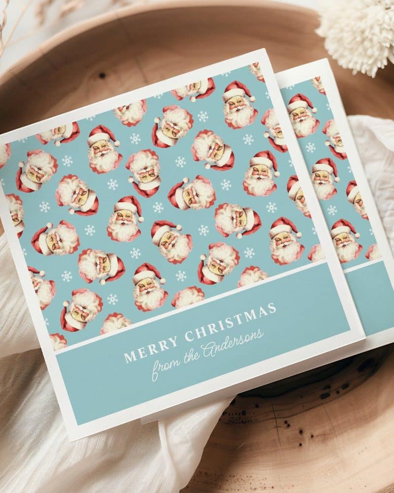 A light blue Christmas card featuring a repeating pattern of Santa Claus faces and snowflakes. The card is personalized with the message Merry Christmas from the Andersons.