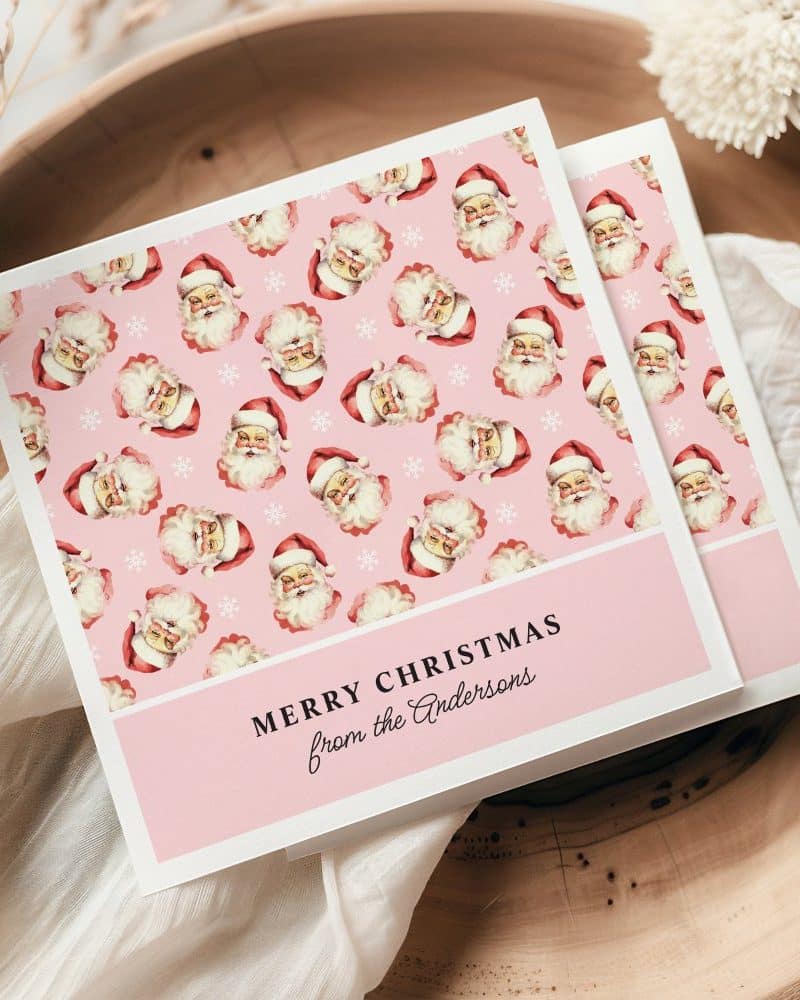 Pink Christmas card with a repeating pattern of Santa Claus faces and snowflakes. The card is personalized with "Merry Christmas from the Andersons."