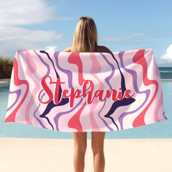 A Woman Holds A Pink, Purple, And Red Beach Towel With The Name Stephanie Written Across It In A Stylized Font.