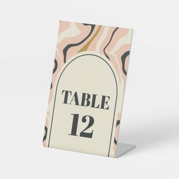 Table Number Twelve, Displayed On A Light Pink And Beige Abstract Patterned Card.