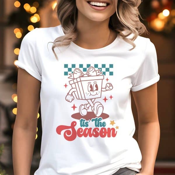 Woman Wearing A White T-Shirt Featuring A Retro Cartoon Gift Character Walking And The Text Tis The Season.