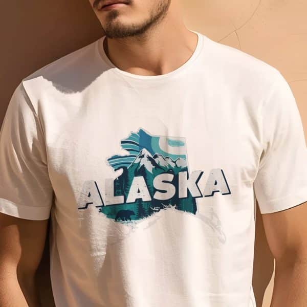 A Man Is Modeling A White T-Shirt Featuring A Teal Graphic Of Alaska'S Outline With Mountains, Trees, And Bears.