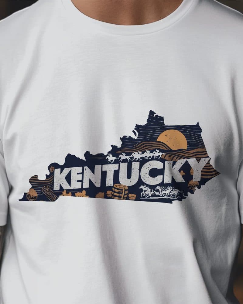 White t-shirt with a navy blue outline of Kentucky, featuring the word Kentucky and imagery of horses and bourbon barrels.