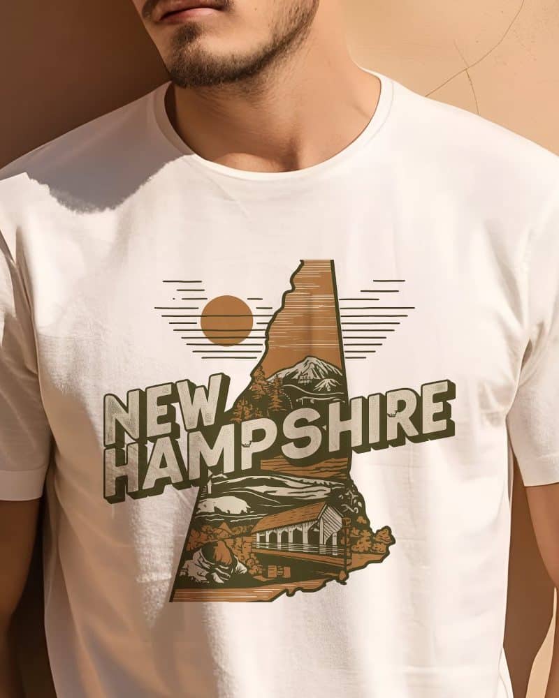 Retro Travel Iconic New Hampshire Graphic T-Shirt Person wearing a white t-shirt with a New Hampshire design. The design features an outline of the state with mountains, a covered bridge, and a stylized sun.