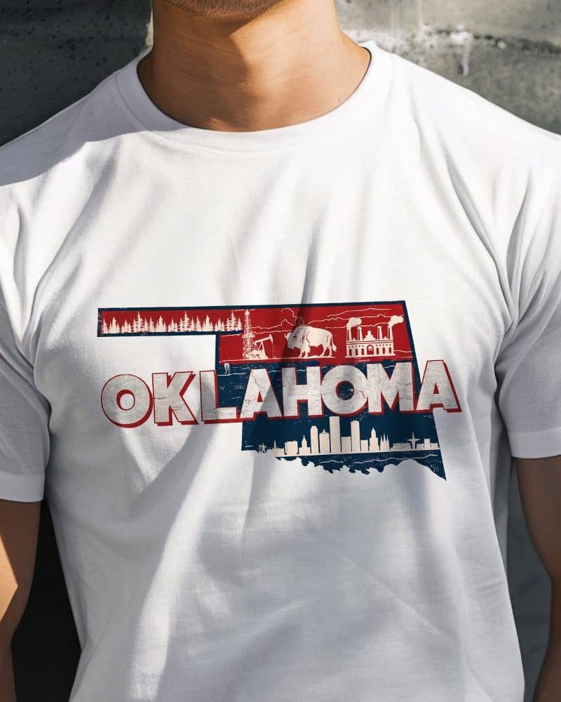 White t-shirt featuring a distressed graphic of the Oklahoma state outline incorporating images representing the state's landscape and industry.