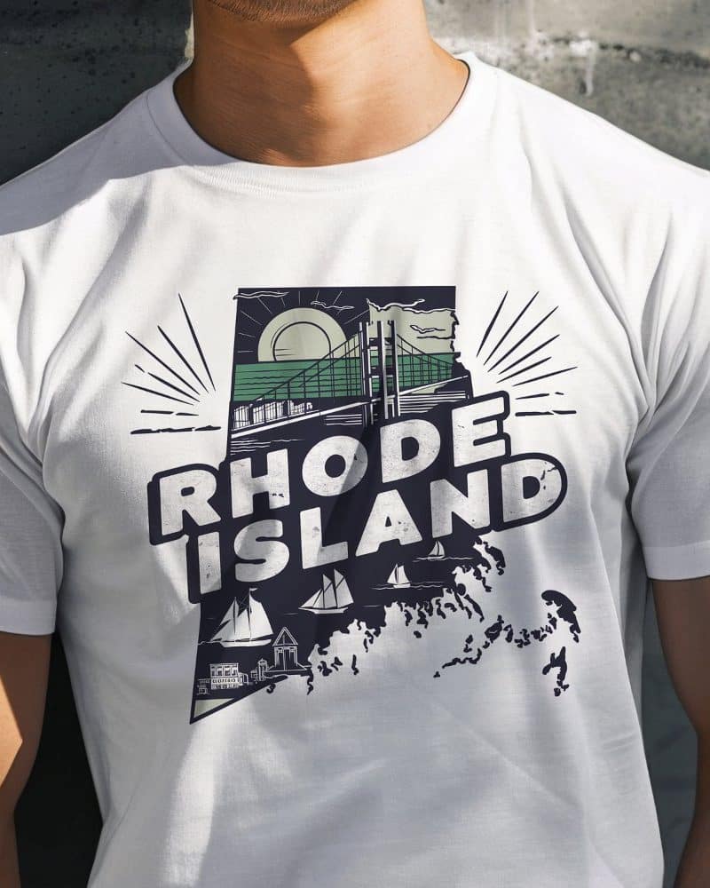 White t-shirt featuring a graphic design of Rhode Island's outline filled with iconic imagery, including a bridge and sailboats. The words Rhode Island are prominently displayed.