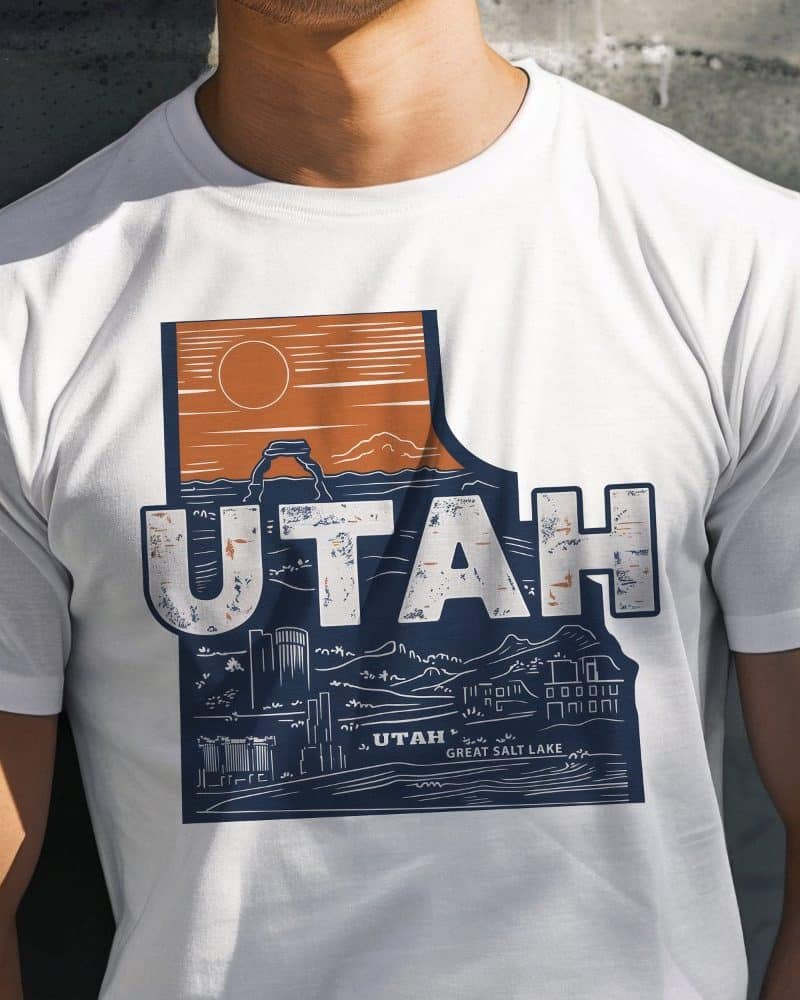 White t-shirt featuring a distressed graphic of the Utah state outline incorporating iconic landmarks and the word Utah.