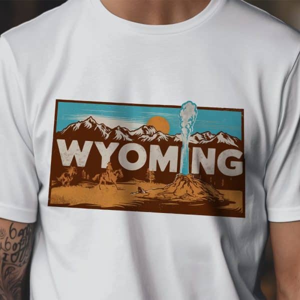 White T-Shirt With A Vintage-Style Graphic Of Wyoming Landscape Featuring A Geyser, Mountains, And Cowboys On Horseback.