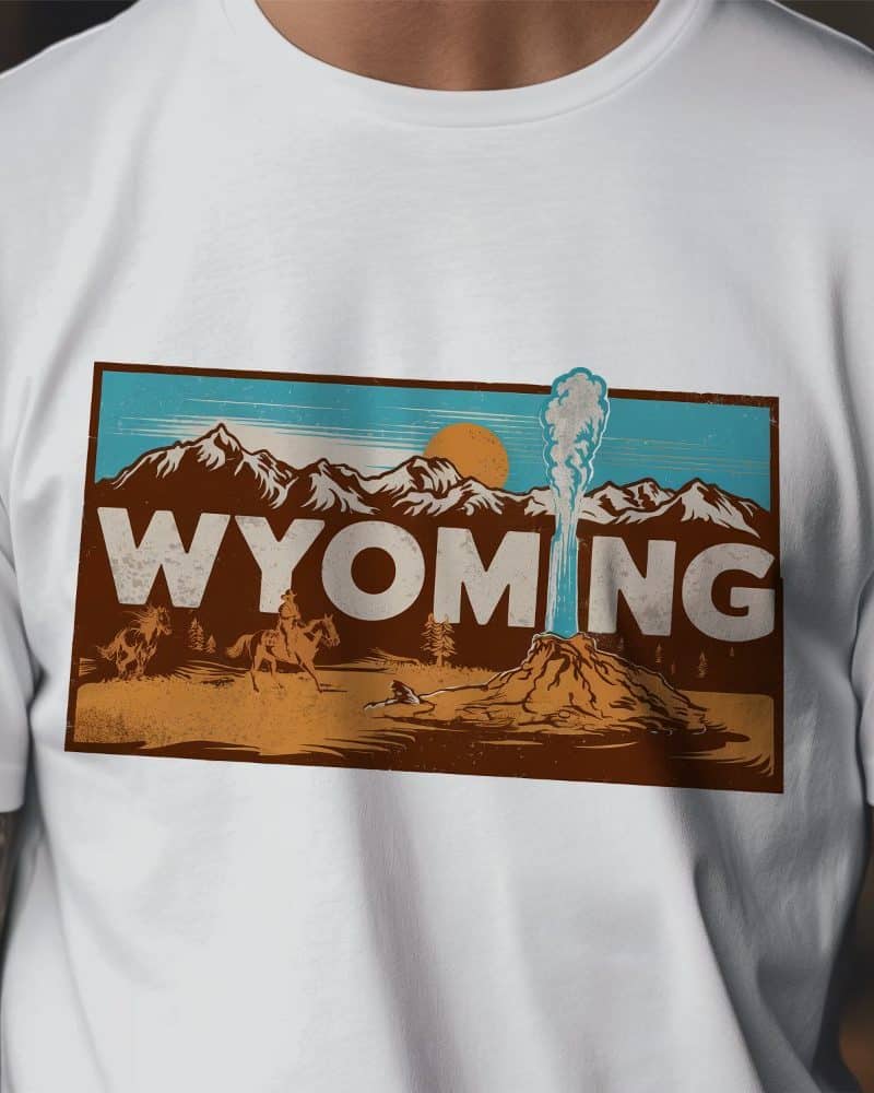 White t-shirt with a vintage-style graphic of Wyoming landscape featuring a geyser, mountains, and cowboys on horseback.