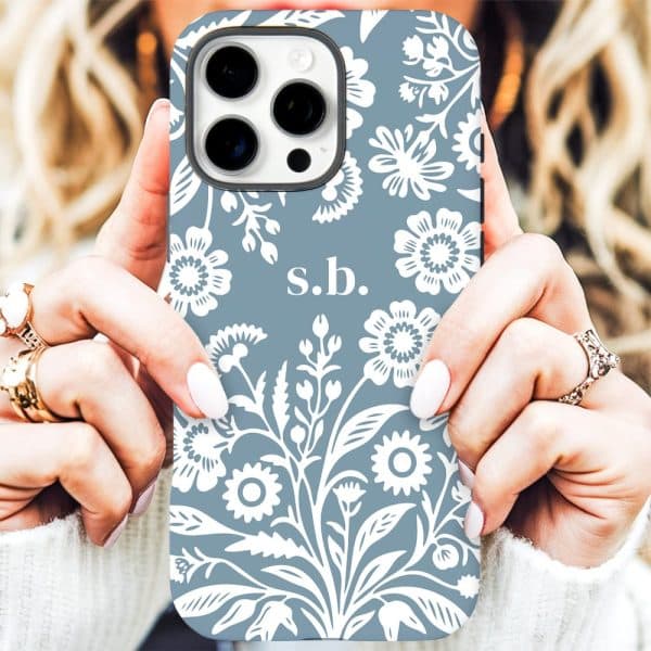 Close Up Of Hands Holding A Light Blue Iphone Case With A White Floral Pattern And Initials S.b.