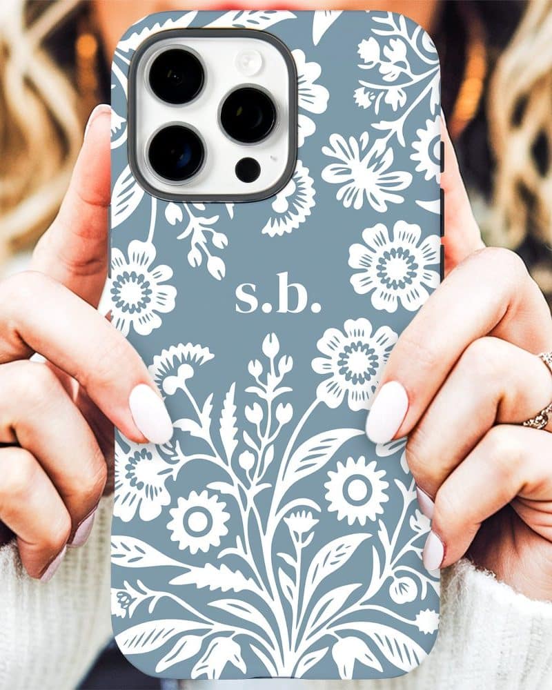 Close up of hands holding a light blue iPhone case with a white floral pattern and initials s.b.