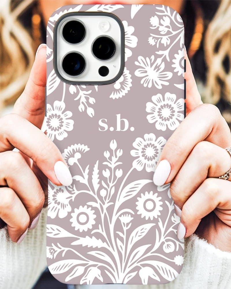 A mauve iPhone case with a white floral pattern and initials s.b.