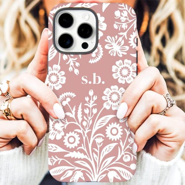 A Person'S Hands Holding A Blush Pink Iphone Case With A White Floral Pattern And The Initials Sb.