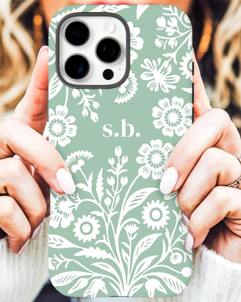 A sage green iPhone case with a white floral pattern and initials s.b. in the center.